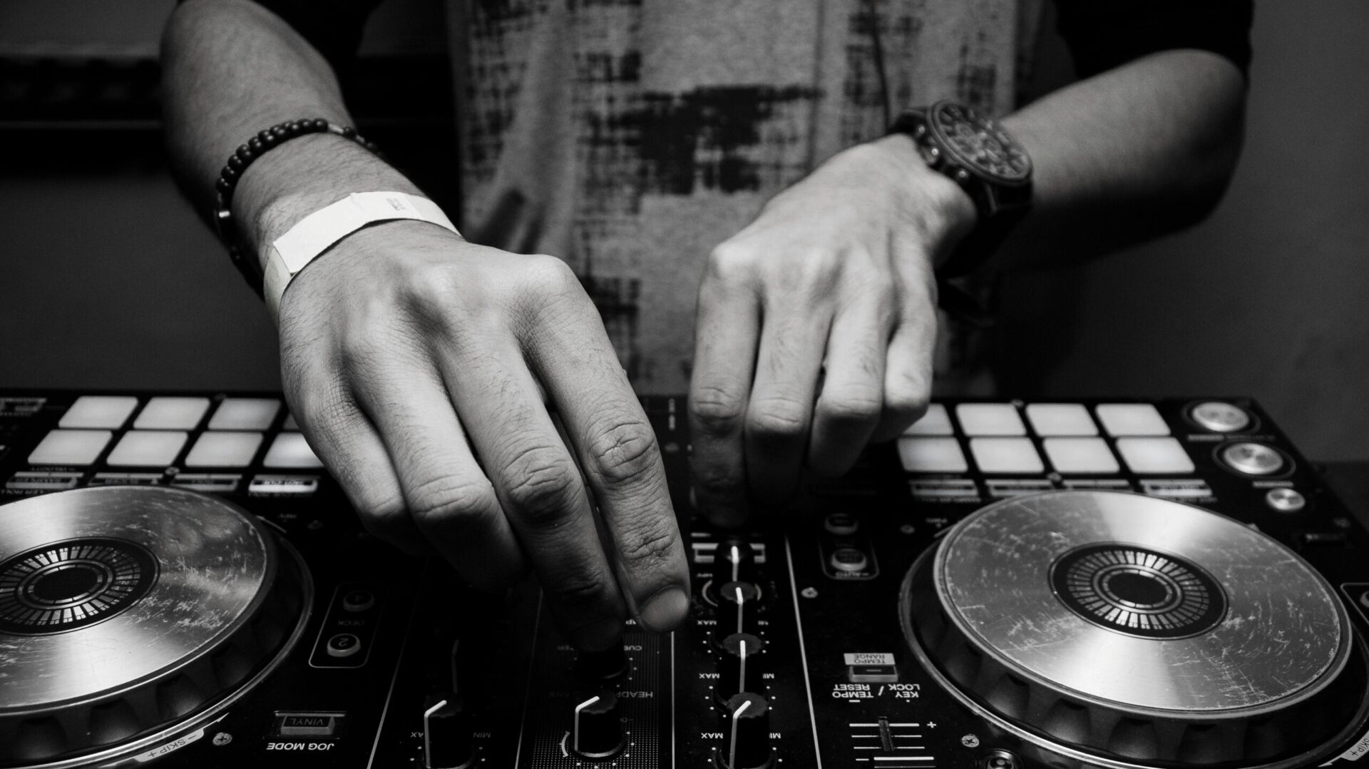 Close-up of a DJ's hands adjusting controls on a mixer in monochrome.
